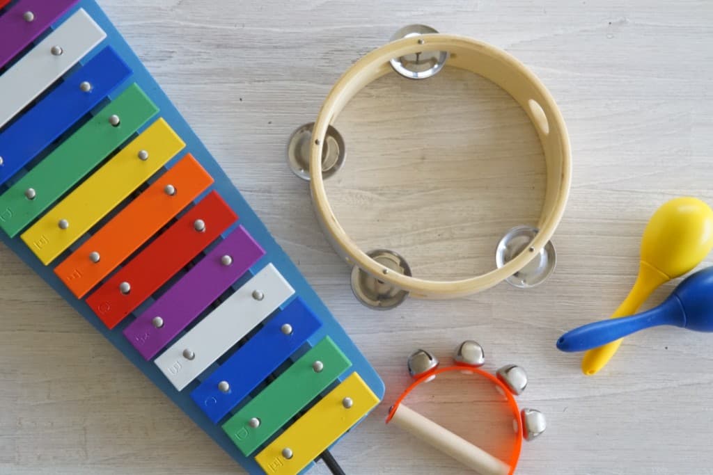 Colourful children's musical instruments including a xylophone, tambourine and maracas on a light wooden surface